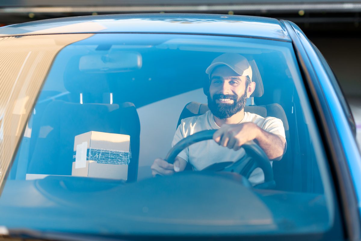 Entregador sorridente com caixa de entrega dentro do carro